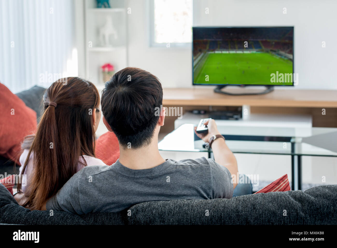 Vue arrière de l'Asian couple regarder le football à la télévision dans la salle de séjour. Festival Football concept. Banque D'Images