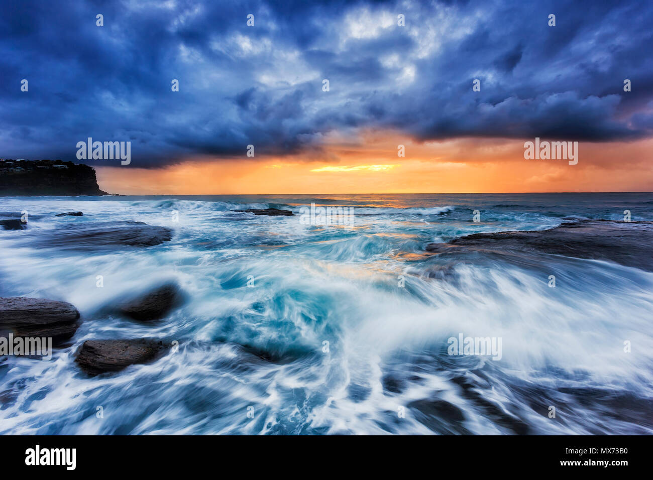 Le temps orageux de l'ouverture de l'océan Pacifique à Bungan beach plages du nord de Sydney avec orange soleil levant sous d'épais nuages. Banque D'Images