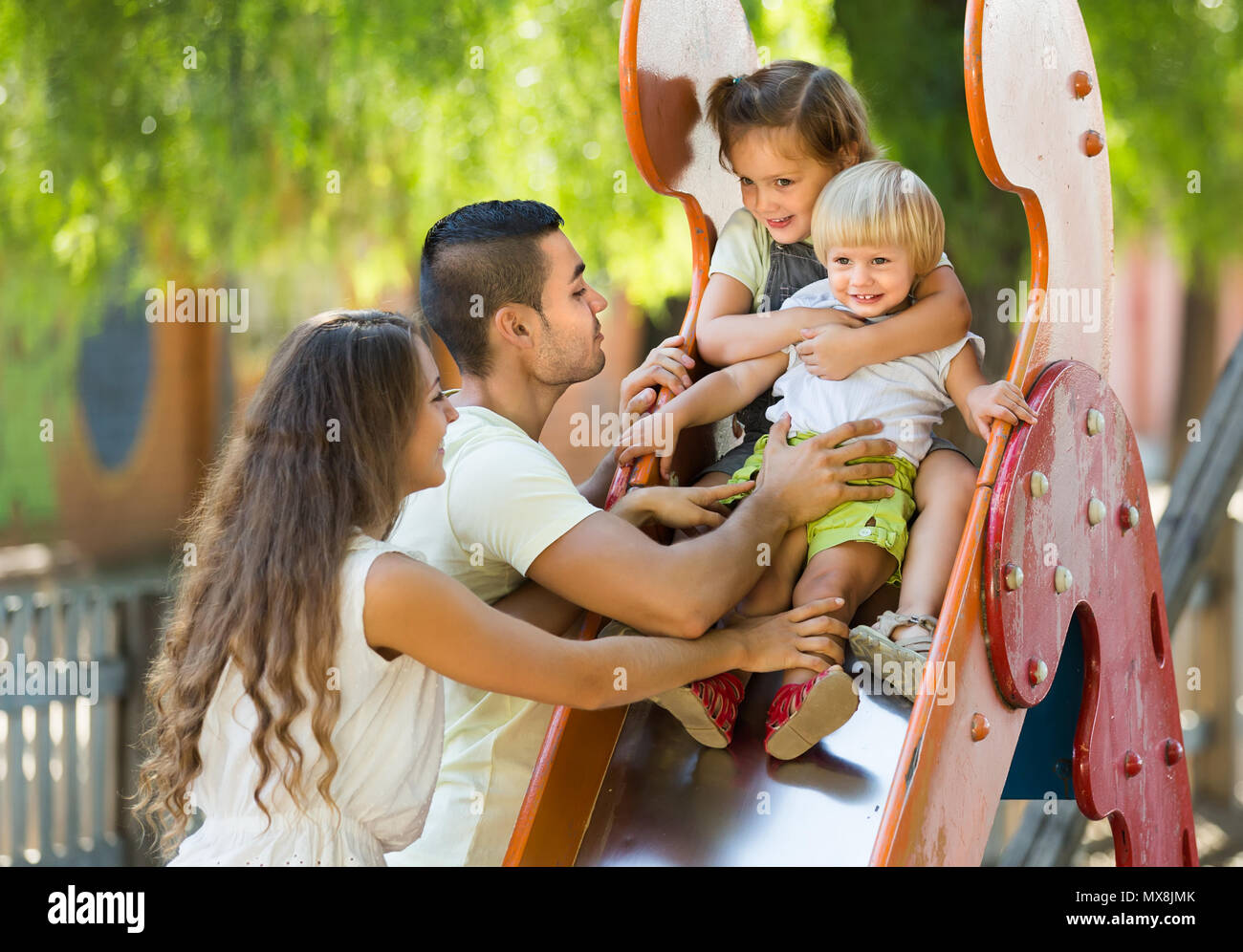 Happy smiling family de quatre à une aire de jeux pour enfants dans le parc. Se concentrer sur la fille Banque D'Images