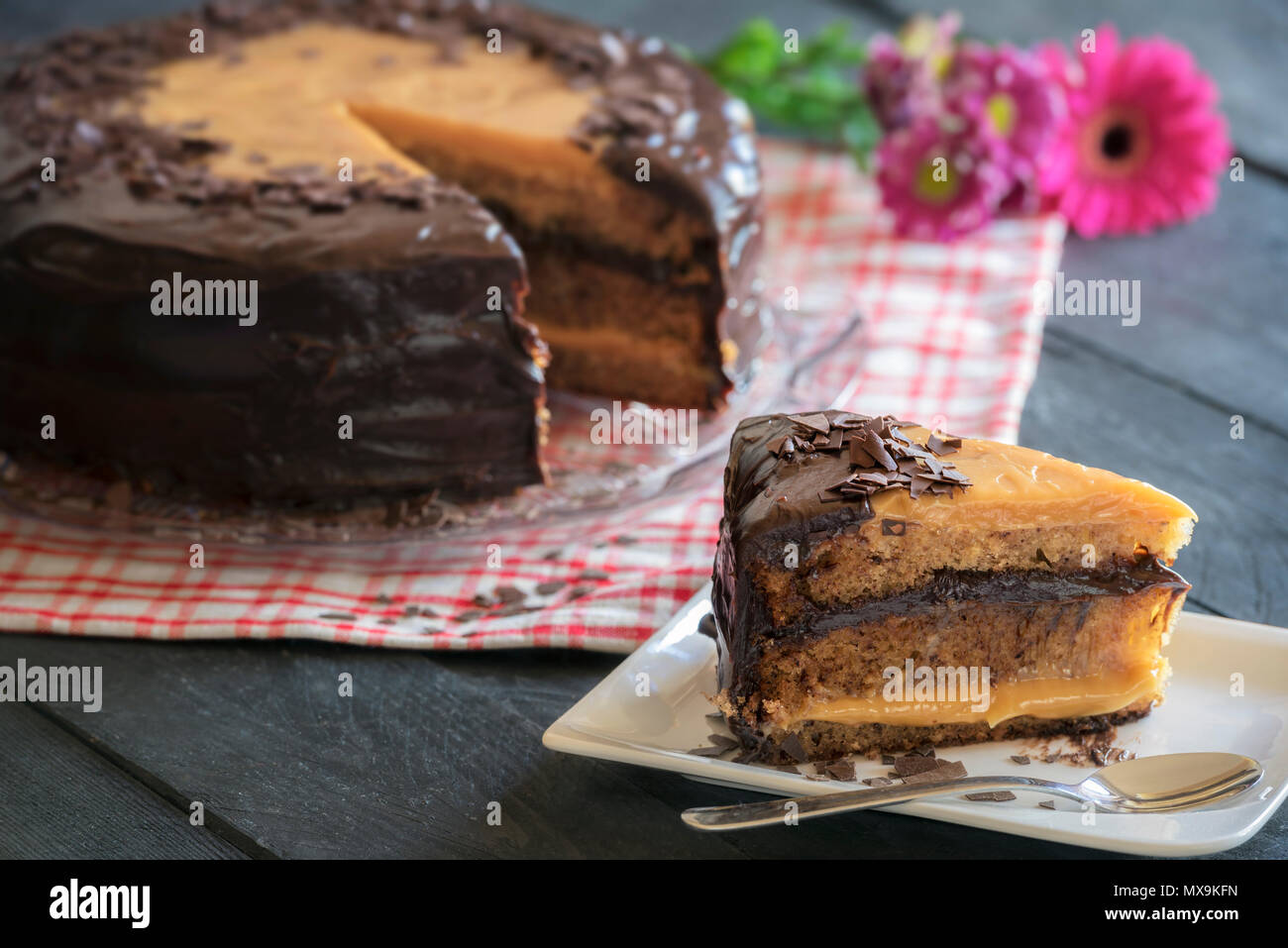 Tranche De Gateau Bresilien Avec Le Lait Et Le Chocolat De Remplissage Brigadeiro Servi Avec De La Creme Fouettee Sur Une Assiette Blanche Et Tissu Du Jute Et Fleurs Jaunes Photo Stock