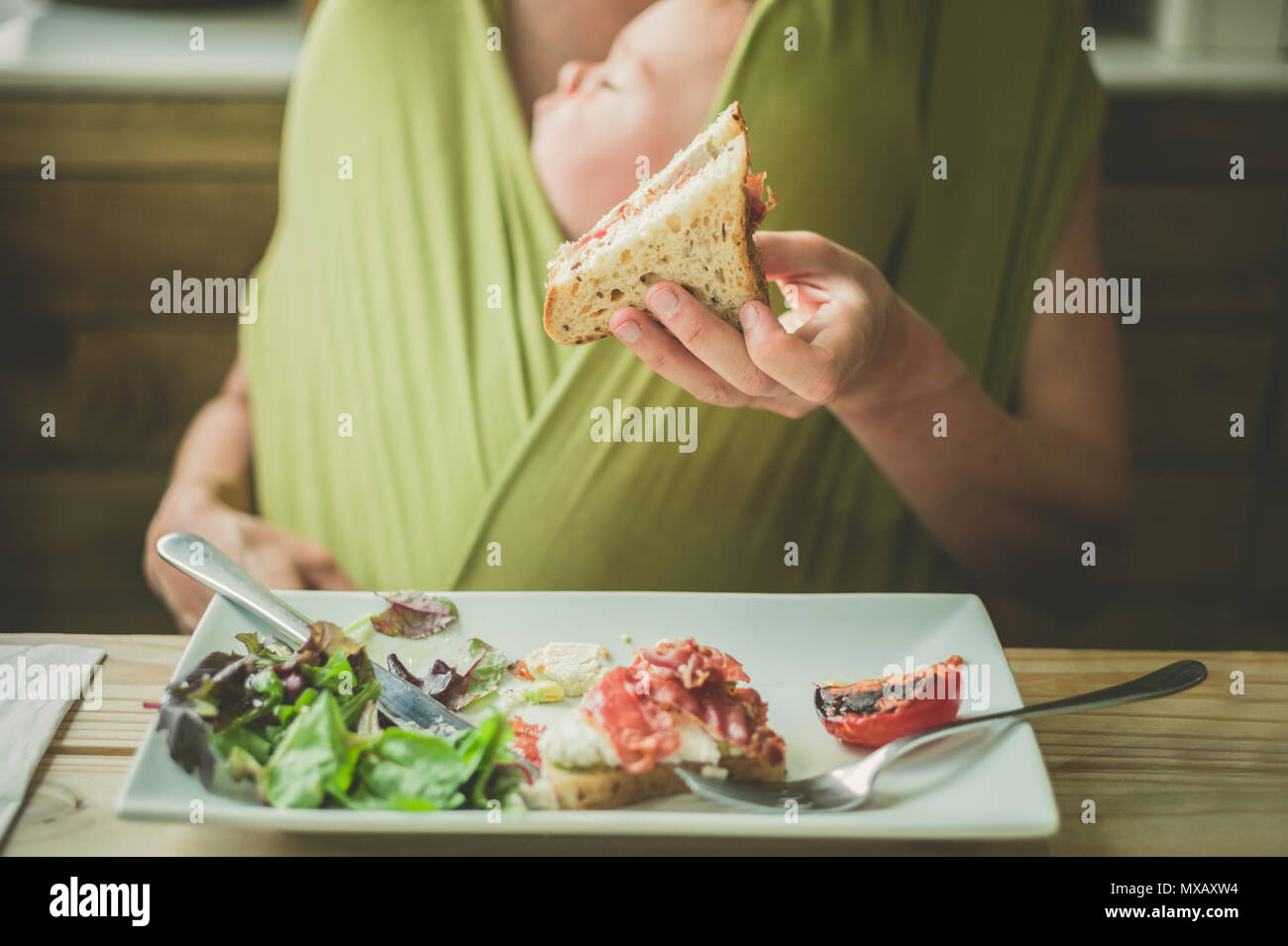 Une jeune mère dans un café est en train de manger un sandwich bacon avec son bébé endormi Banque D'Images
