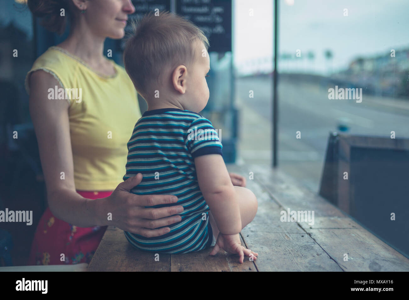 Un yougn mère et son bébé sont assis dans un café et regarder par la fenêtre Banque D'Images