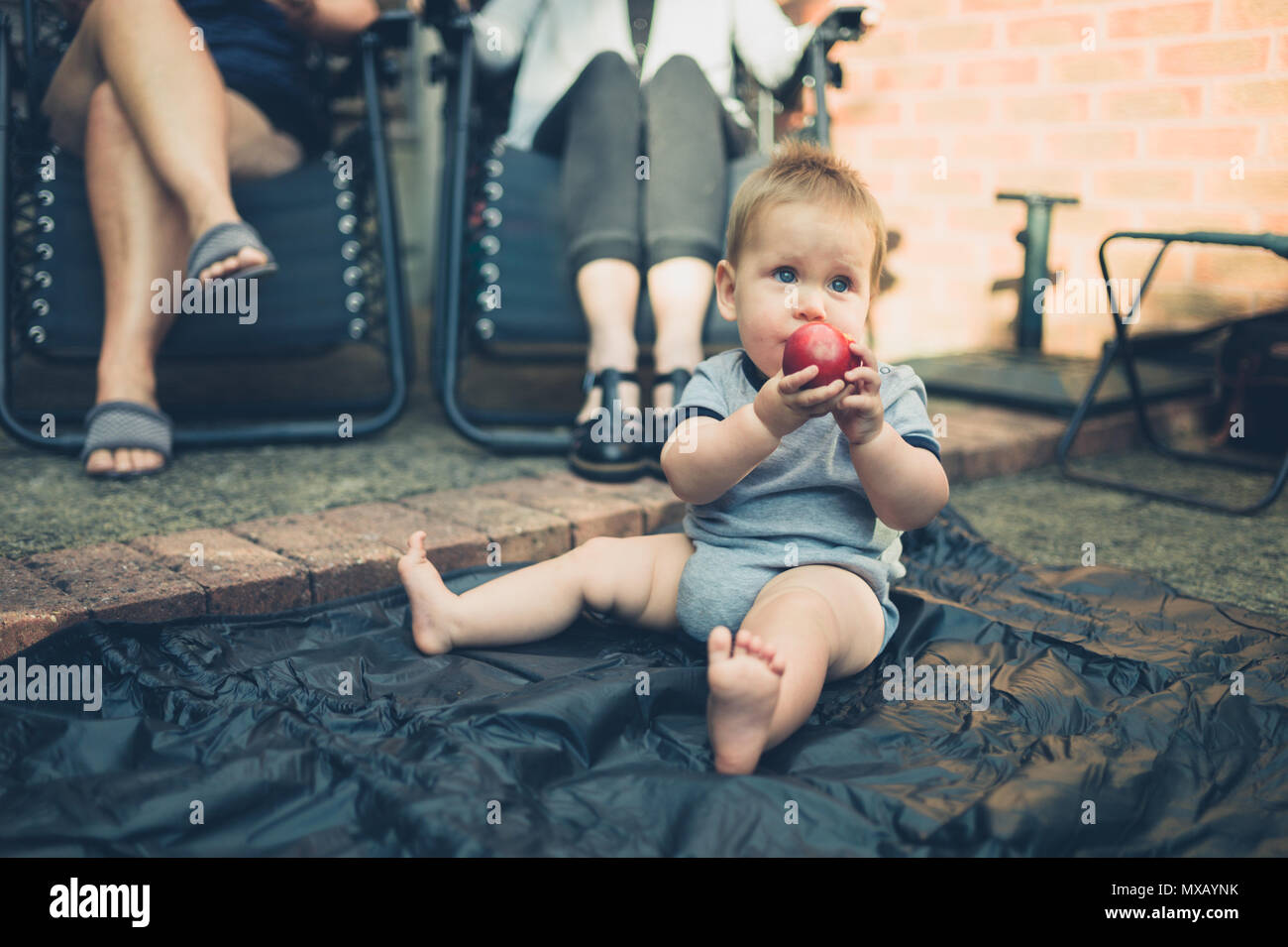 Un Mignon Petit Bebe Est Assis Sur Le Sol Dans Le Jardin Et Est En Train De Manger Une Peche Photo Stock Alamy