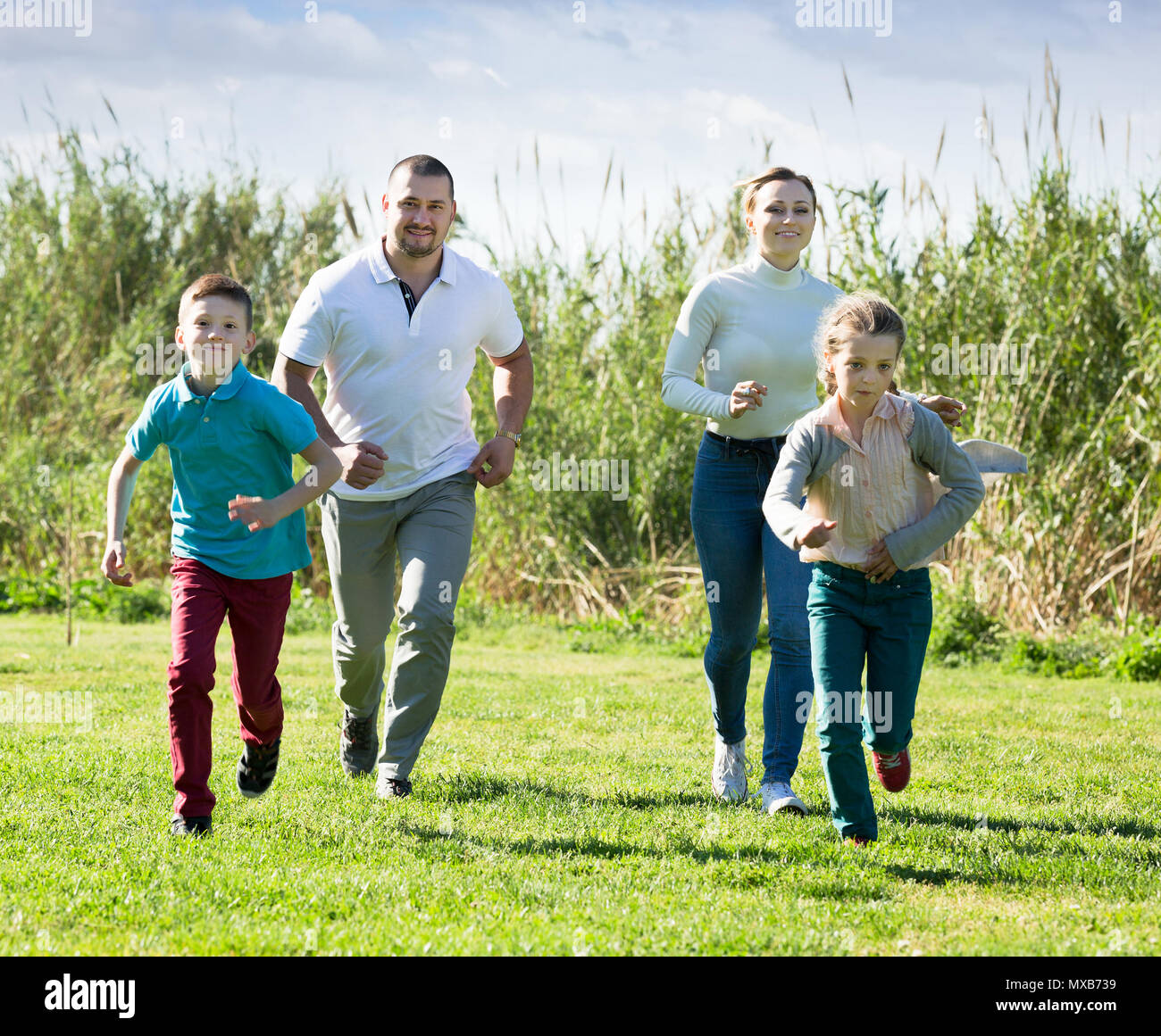 Souriante jeune famille de quatre personnes heureusement jouer et courir ensemble à l'extérieur Banque D'Images
