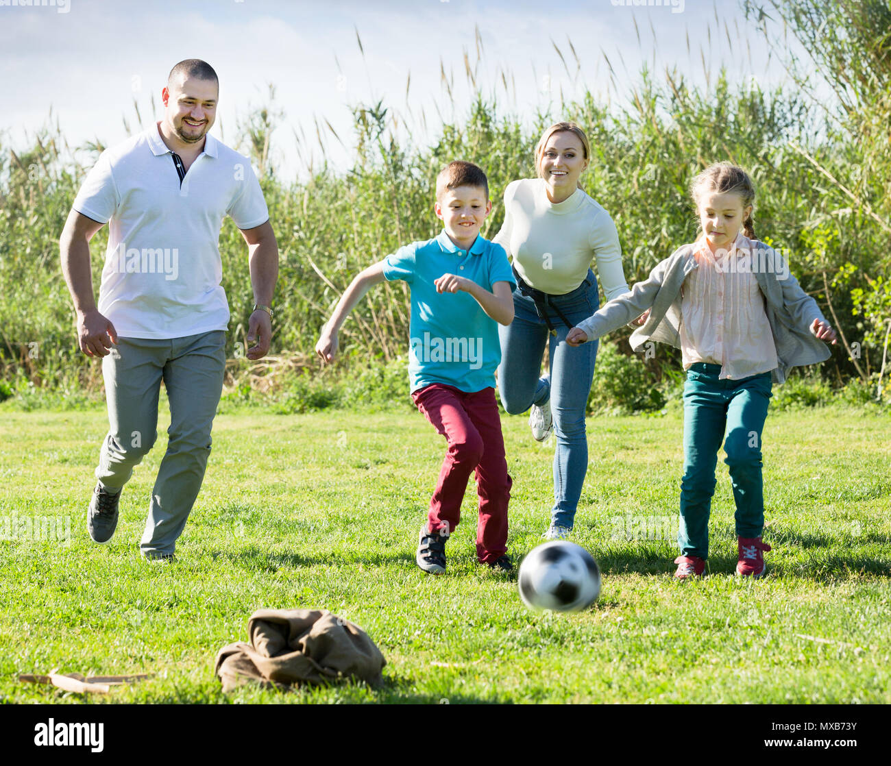 Famille de quatre personnes jouant joyeusement dans le football et rire ensemble à l'extérieur Banque D'Images