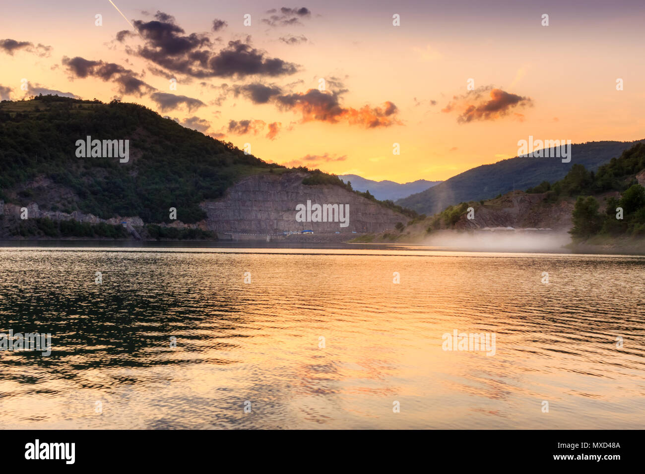 Golden sky et spectaculaire sur les nuages moelleux, soyeux réfléchissants lake et nuage de poussière volant au-dessus de l'eau de la route Banque D'Images