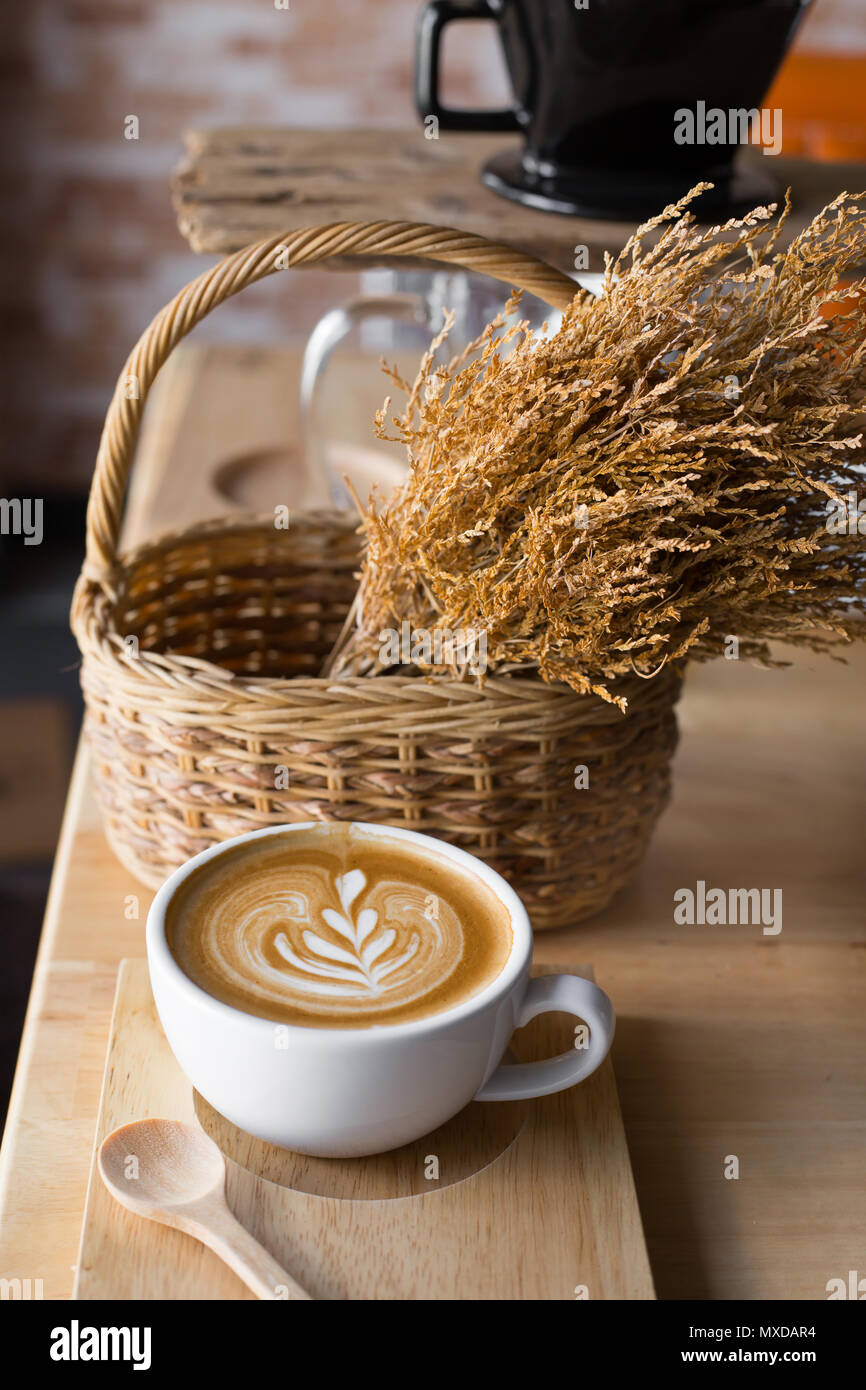 Une tasse de café latte avec les fleurs séchées dans le panier sur la table de bois. Banque D'Images