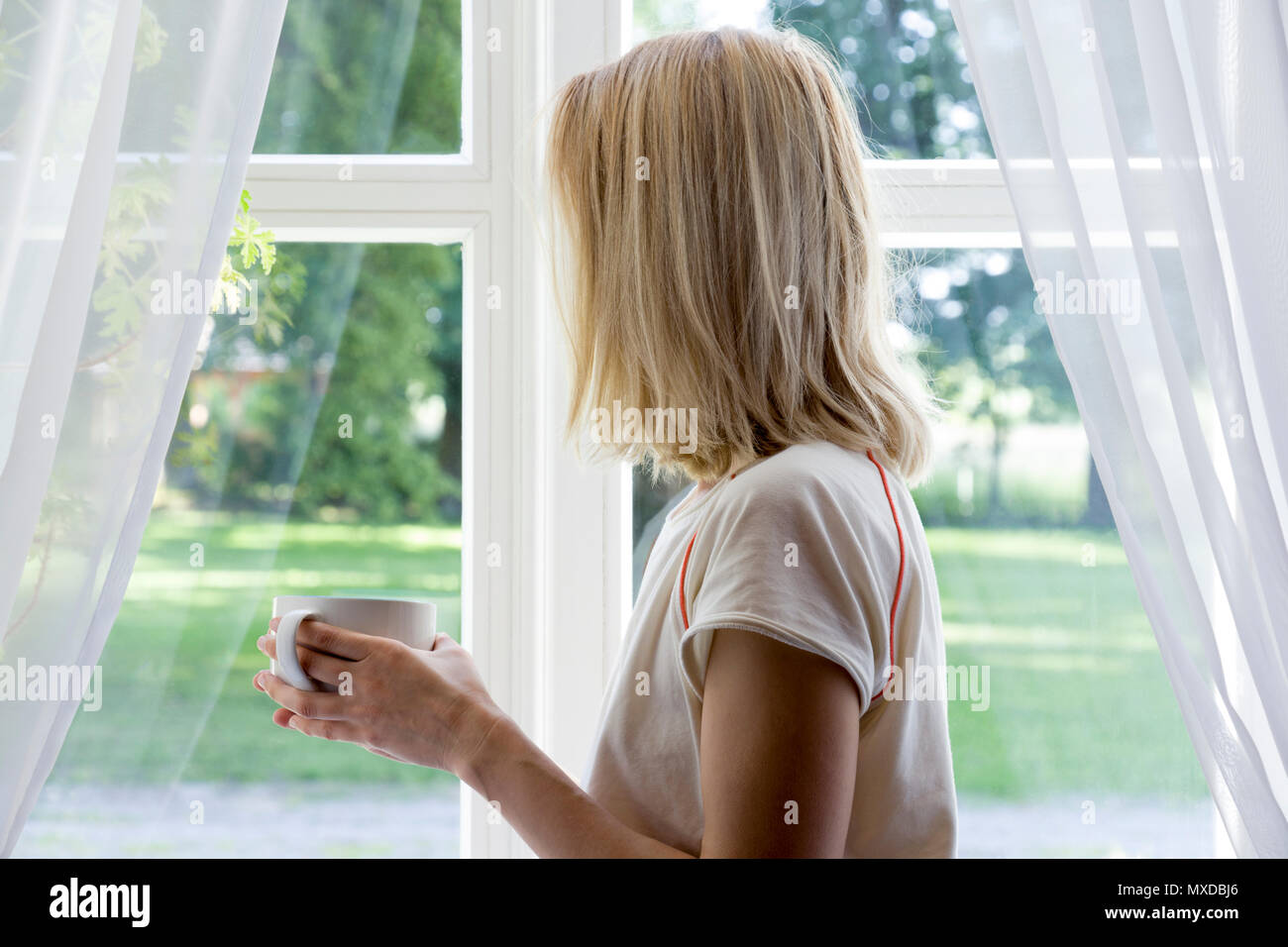 Jeune fille profitant de son café du matin ou le thé, en regardant par la fenêtre. Banque D'Images