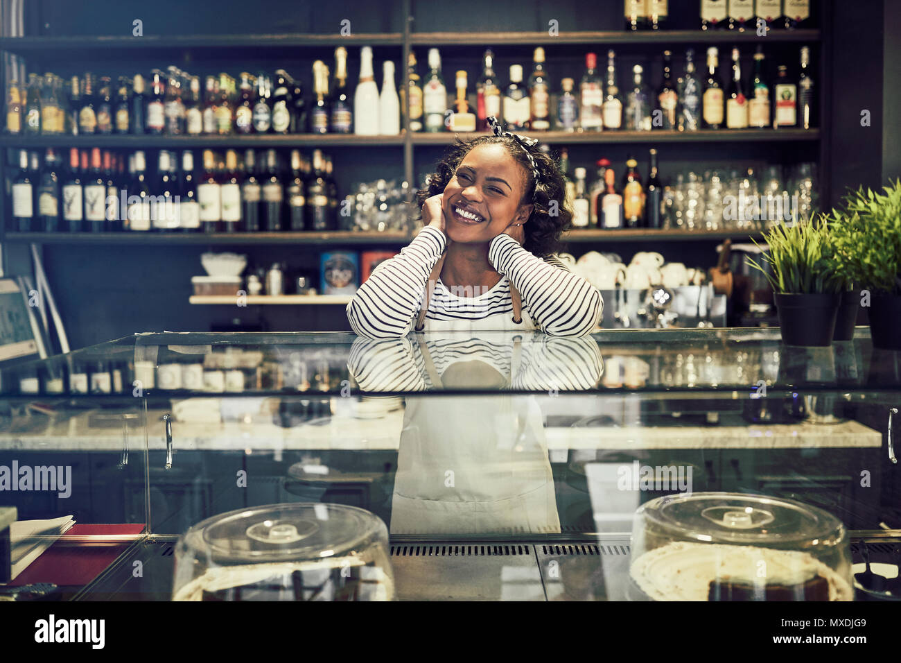 Souriante jeune entrepreneur africain portant un tablier et debout derrière le comptoir de son café à la mode Banque D'Images