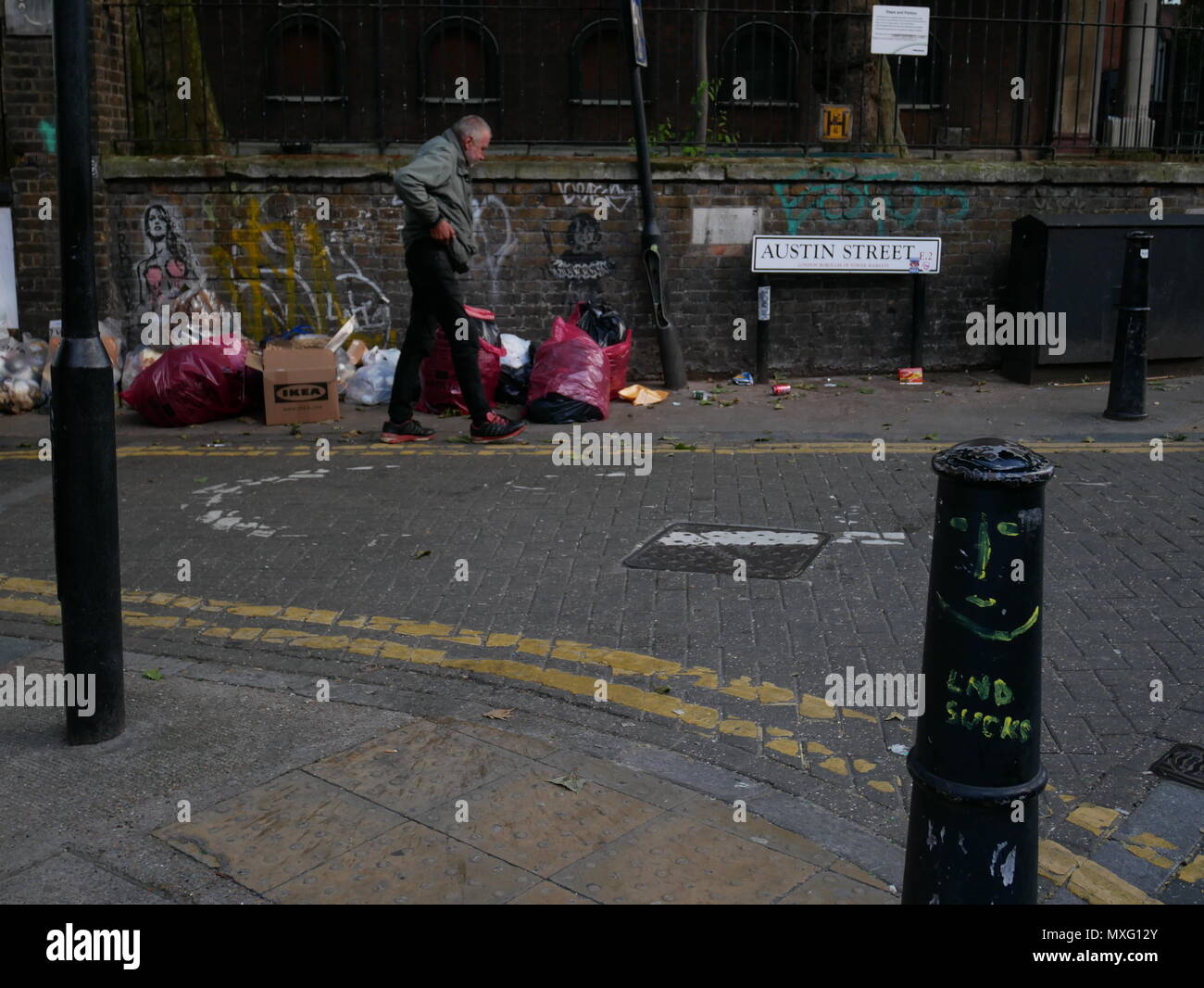 Un sans-abri marche dernières sacs de détritus à l'extérieur de St Leonards Church of England, Shoreditch, London. Banque D'Images