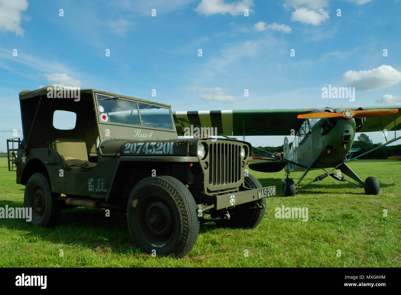Avion et voiture vintage. Avion Piper Cub du jour J en temps de guerre avec l'US Willys Jeep. Willys MB véhicule de guerre. Champ d'herbe. Rayures d'invasion Banque D'Images