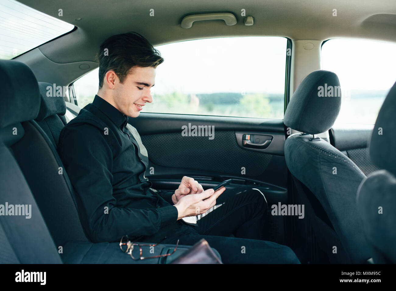 Un jeune, beau garçon d'adolescent est assis sur un siège de voiture de tourisme et décide par téléphone Banque D'Images