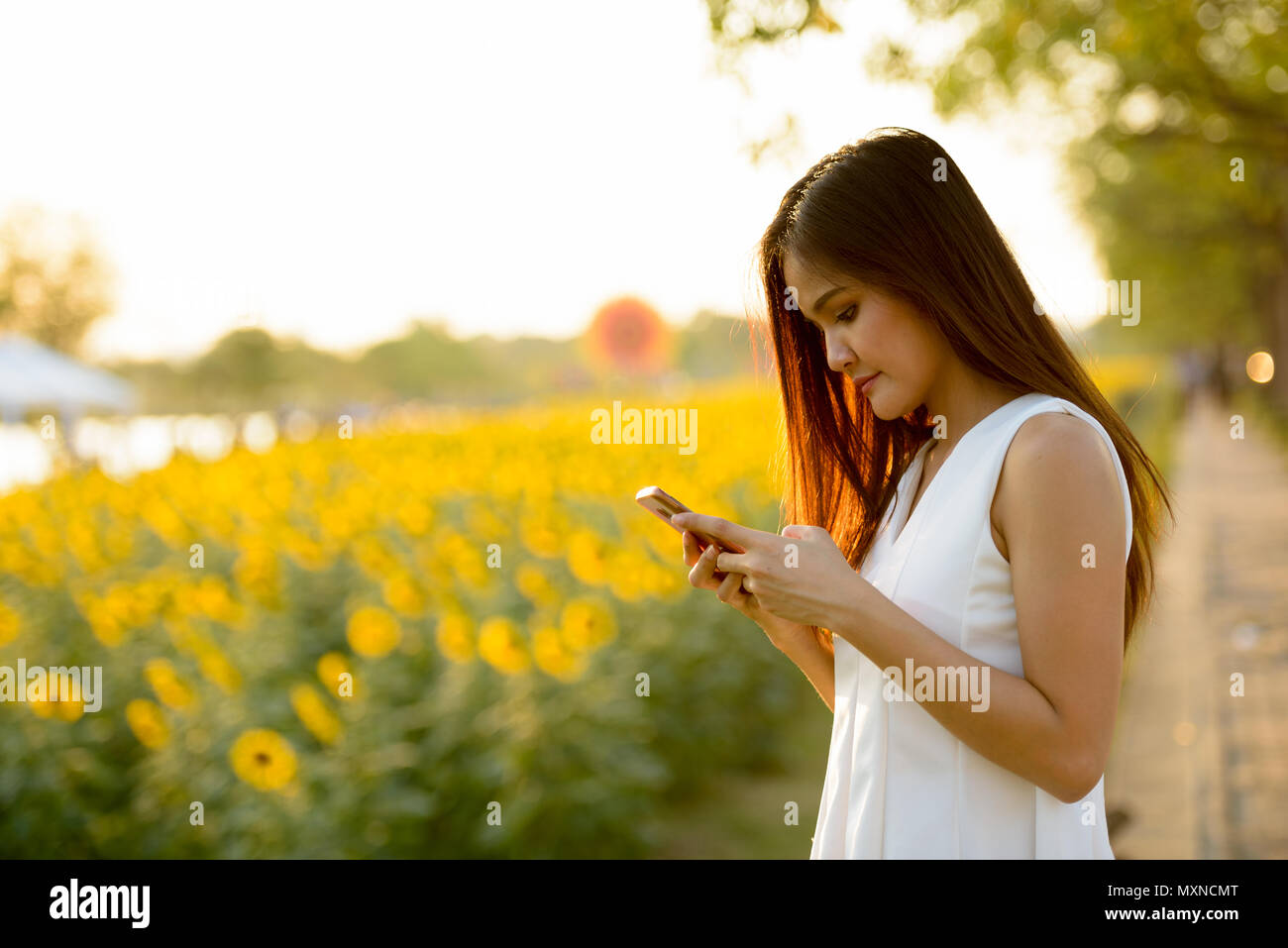 Belle jeune femme asiatique à l'aide de téléphone mobile contre un champ de Banque D'Images