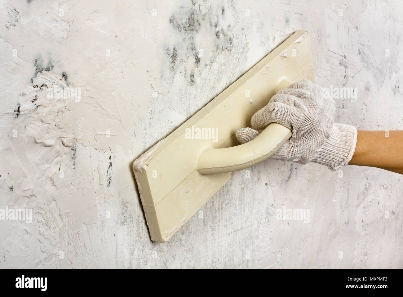 La main avec une truelle de lissage et de plâtrage de mur de béton durant la réparation Banque D'Images