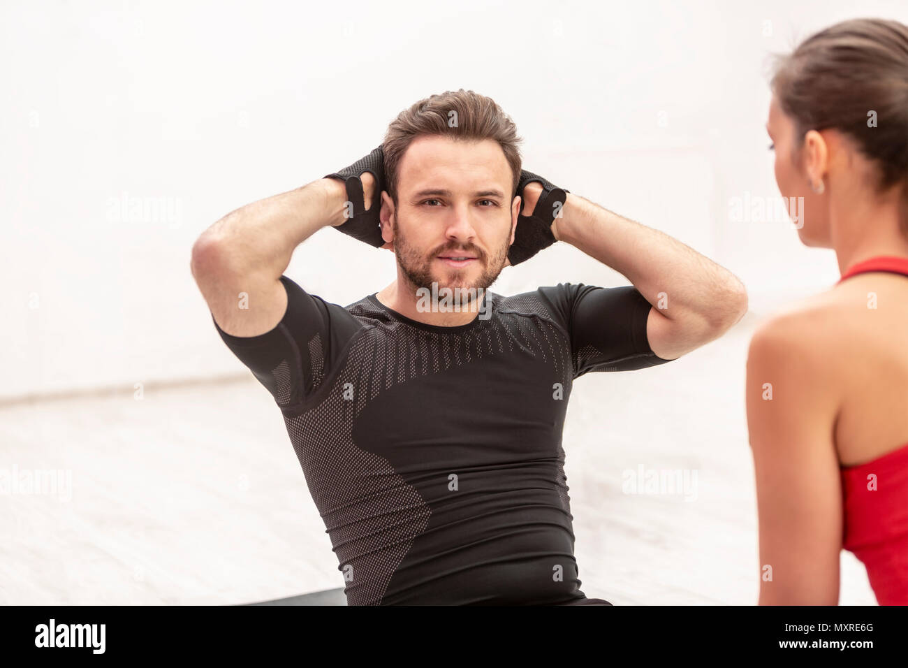 Jeune homme de faire des redressements assis sur le sol dans une salle de sport avec sa femelle formateur. Banque D'Images