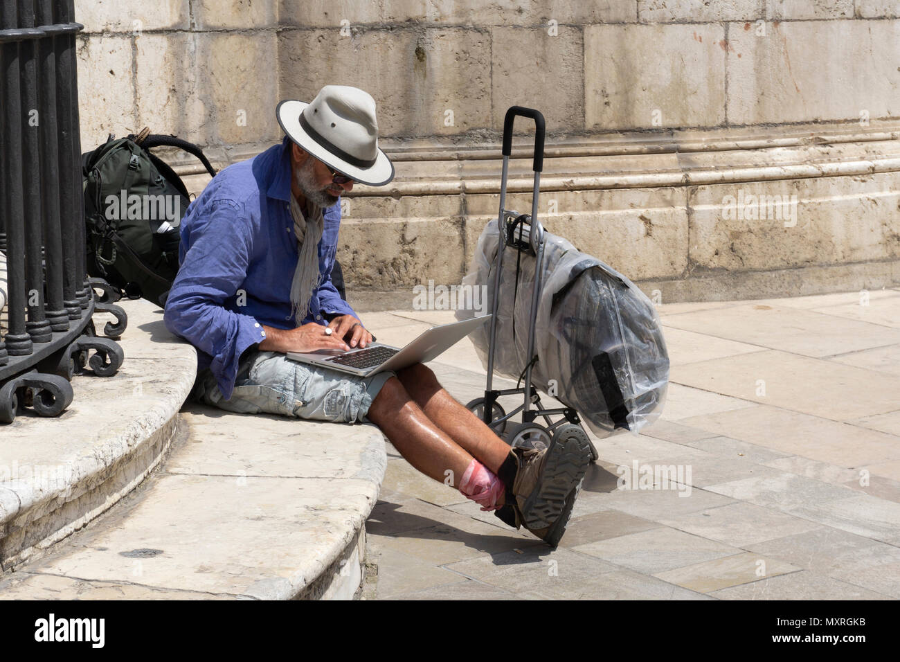 Maison de vacances traveler en utilisant lap top man wearing hat short sac à dos assis étapes malaga Banque D'Images