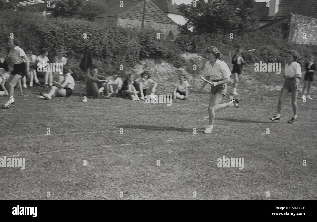 1960, tableau historique des écolières secondaires prenant part à une course de relais dans un comté inter-écoles sports le jour, Dorset, England, UK. Une des filles est montré transportant le relais baton dans sa main gauche tout en courant aussi vite qu'elle le peut sur la piste d'herbe. Banque D'Images