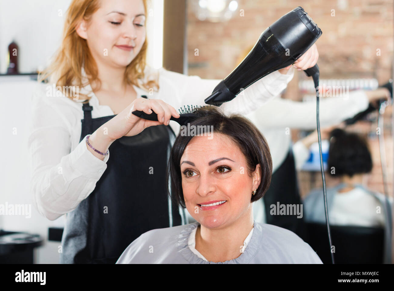 Les jeunes satisfaits coiffure styling et sécher les cheveux avec fen et la brosse  de femmes dans un salon de beauté Photo Stock - Alamy