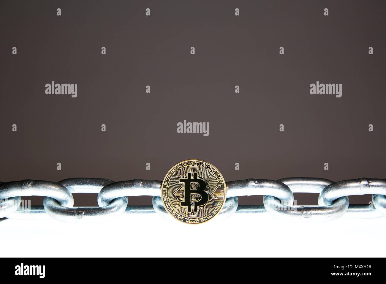 Un Bitcoin est situé sur une surface brillante blanc tandis qu'une chaîne en métal acier lourd se trouve derrière. Concepts de la technologie de la chaîne d'bloc et la monnaie numérique. Banque D'Images