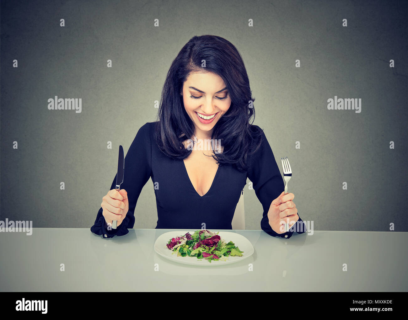 Belle brune assise à table et à la plaque avec une salade avec excitation à avoir une alimentation saine pour perdre du poids Banque D'Images