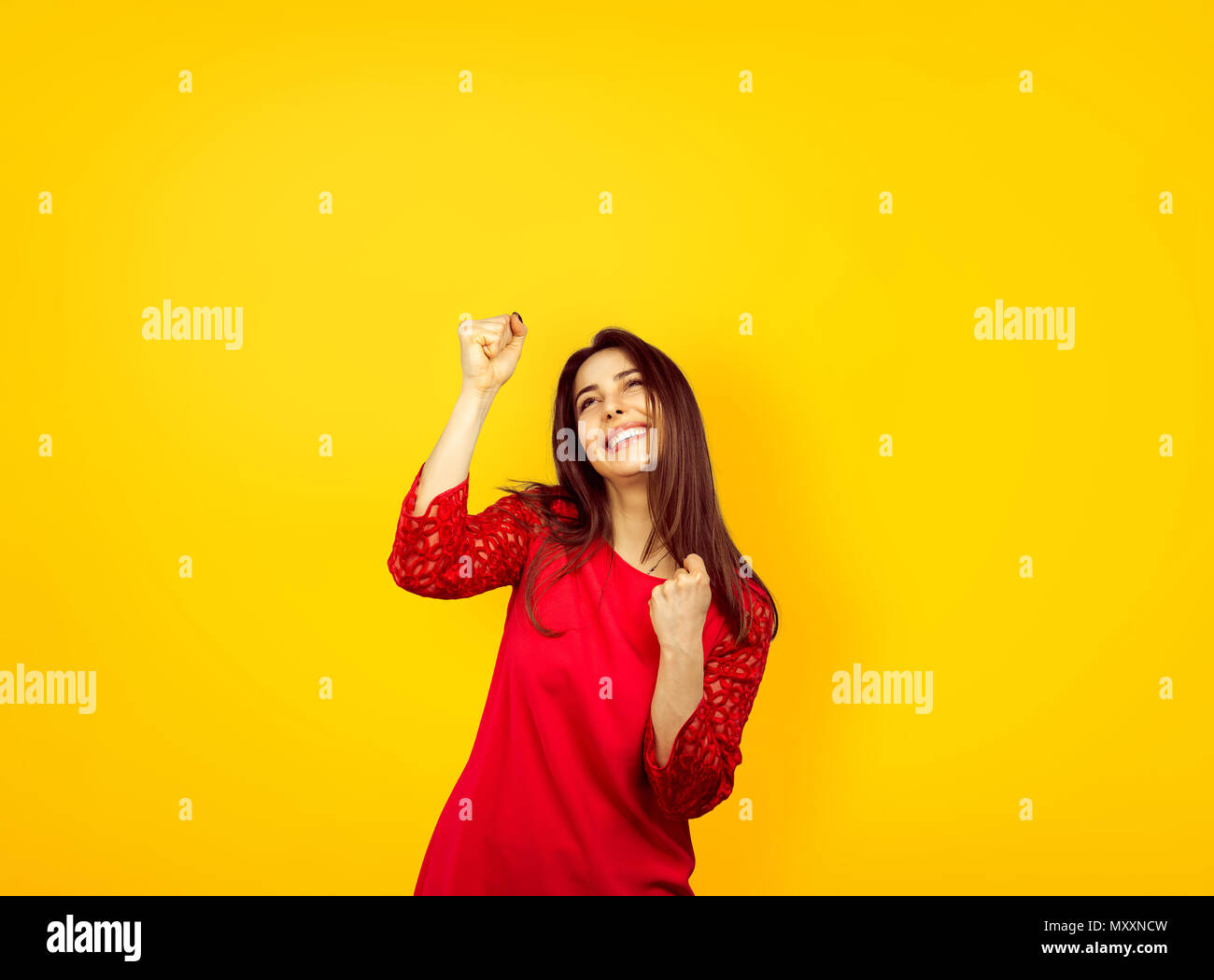 Trendy brunette en robe rouge à la super étonné avec succès et à célébrer la victoire avec hands up Banque D'Images