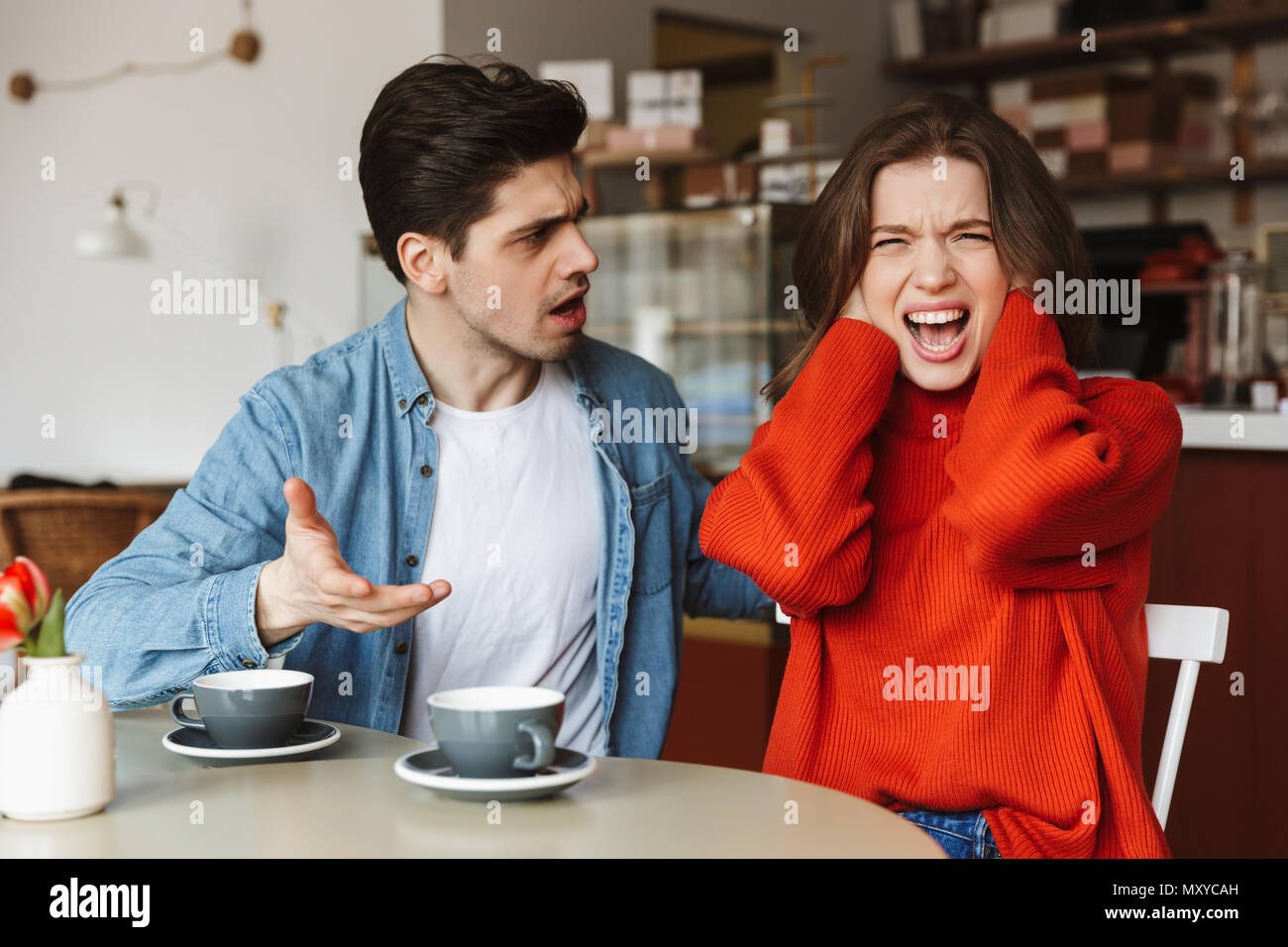 Déçu couple homme et femme 20s de crier et d'avoir à redire tout en ayant pause café dans cafe Banque D'Images
