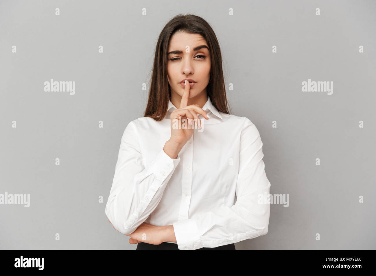 Image de femme brune 20s dans l'Habillement formel tenant l'index sur les lèvres et lui demandant de garder le silence sur fond gris isolé Banque D'Images