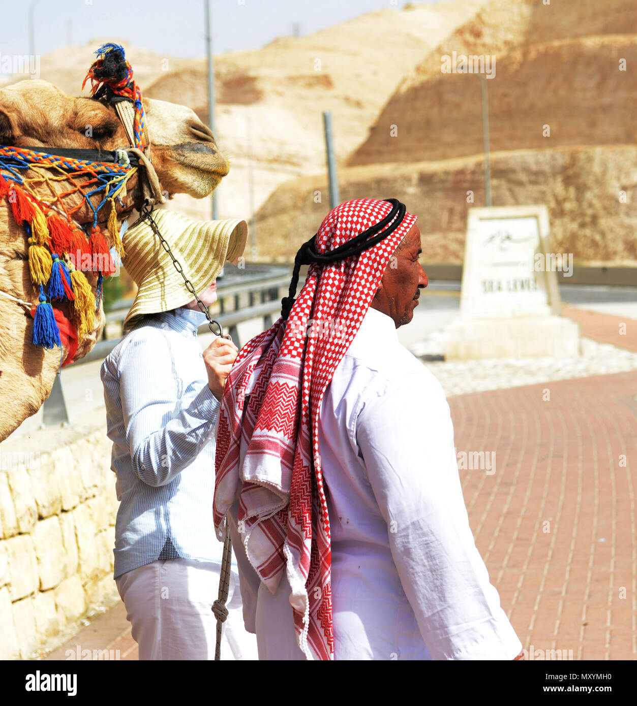 Un touriste posant pour une photo avec un Bédouin l'homme et son chameau au niveau de la mer sur la route menant à la mer Morte en Israël. Banque D'Images