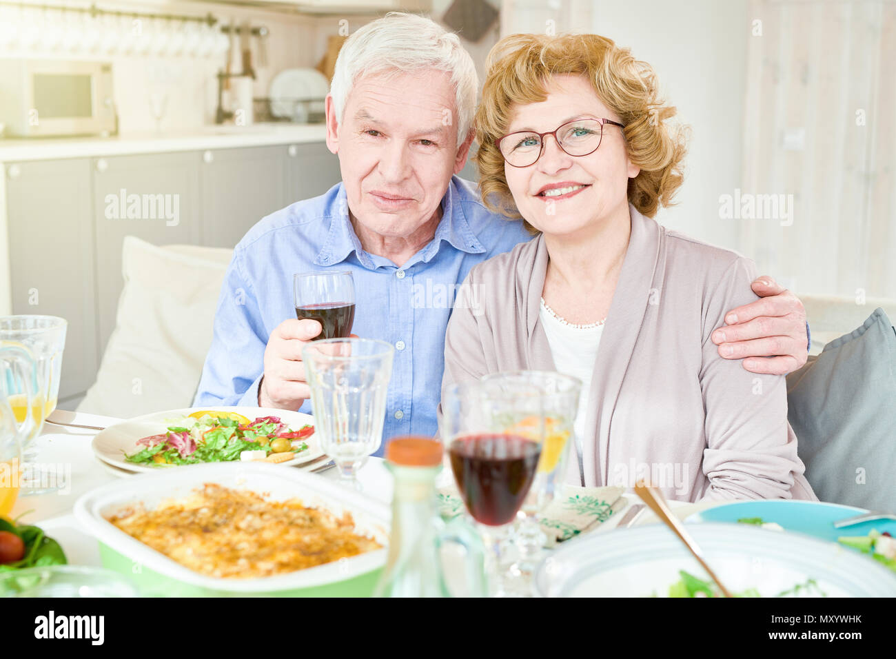 Portrait of happy senior couple at dinner table smiling and looking at camera lors de fête de famille à la maison Banque D'Images
