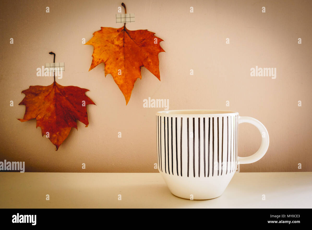 Mug blanc avec des lignes noires décorations sur un tableau blanc avec deux feuilles d'automne sur l'arrière-plan. Concept d'automne. Look Vintage filtre. Banque D'Images