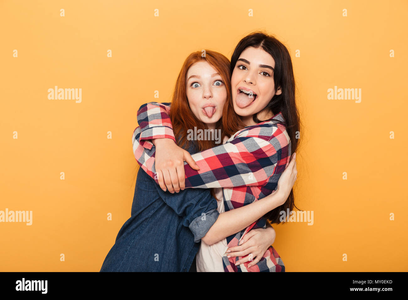 Portrait de deux jeunes adolescentes drôle hugging and looking at camera isolated sur fond jaune Banque D'Images