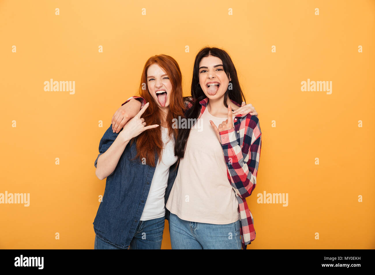 Portrait de deux jeunes adolescentes drôle montrant cornes jusqu'à la gestuelle et à huis clos sur fond jaune isolé Banque D'Images