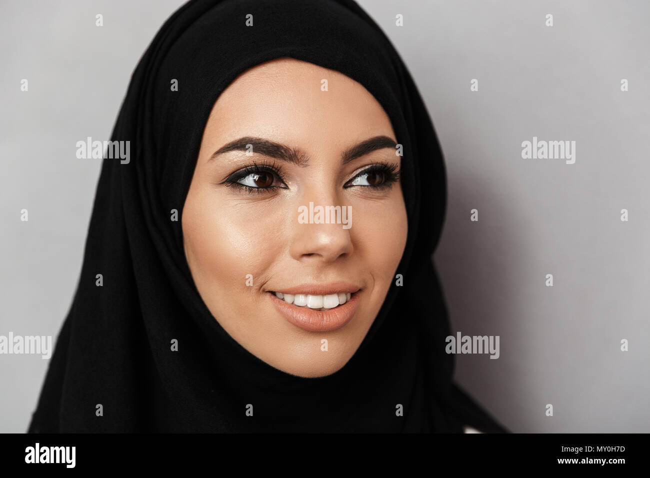 Gros plan Portrait de la prière musulmane femme 20s en foulard religieux avec maquillage oriental et souriant à côté fond gris plus isolés Banque D'Images