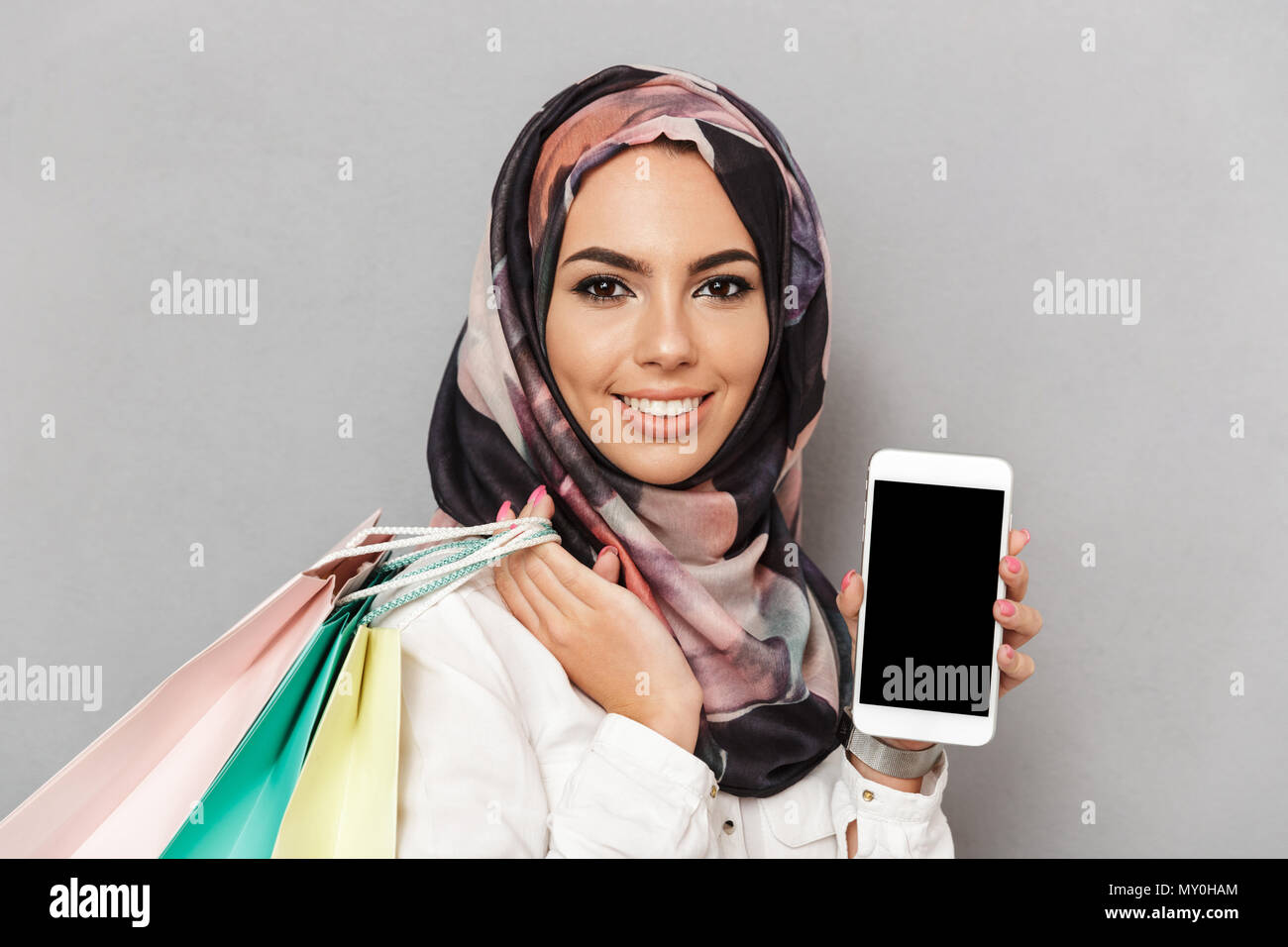 Portrait d'une jeune femme arabe montrant écran blanc téléphone mobile de fond gris Banque D'Images