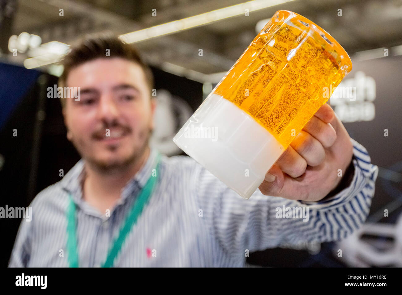 05 juin 2018, l'Allemagne, Erfurt : Arthur Morche de la société Prototech Asia holding envers un verre avec une bière-comme remplir faite de polyuréthane au cours de la 15e FabCon.Tech rapide 3.D juste à Erfurt. Les objets en 3D peuvent être produites par l'injection d'un matériau polyuréthane dans un moule en silicone. Les exposants présentent leurs nouveaux produits et applications dans le domaine de la fabrication additive et l'impression 3D entre 05 et 07 juin. Photo : Christoph Soeder/dpa Banque D'Images