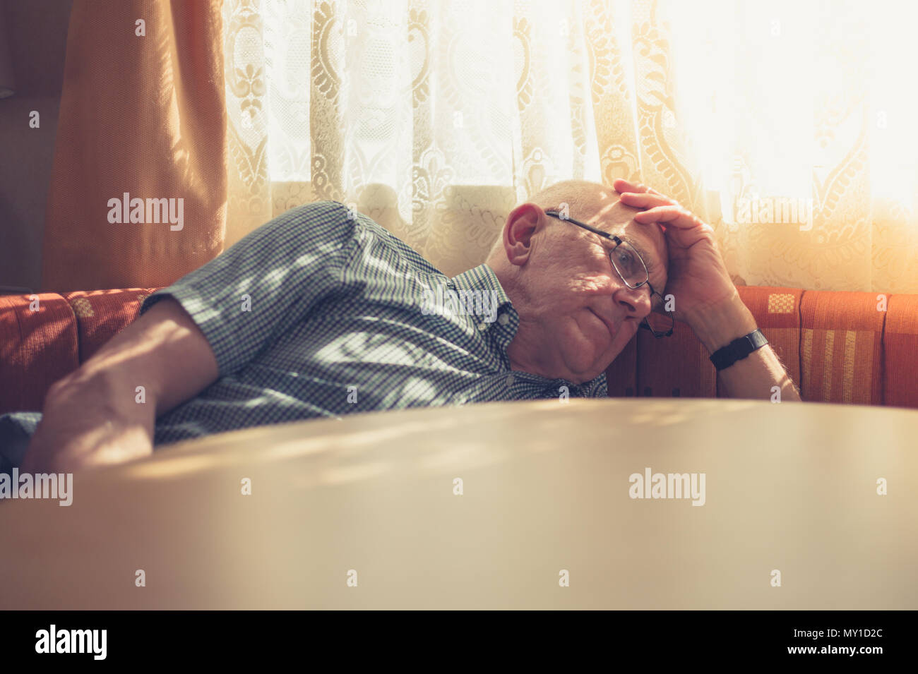 Un vieil homme triste et fatigué se repose sa tête par la fenêtre au soleil Banque D'Images