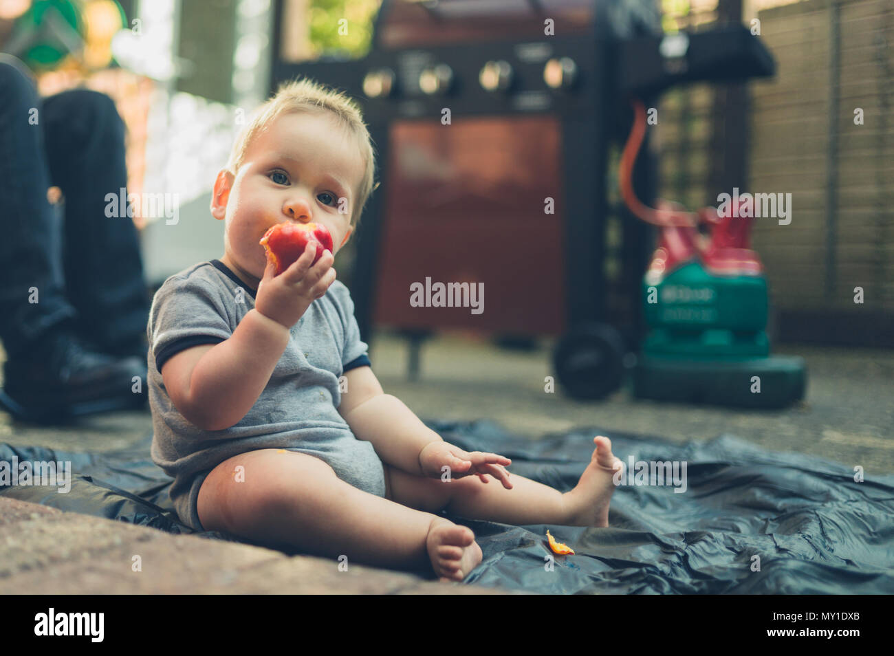 Un Mignon Petit Bebe Est Assis Sur Le Sol Dans Le Jardin Et Est En Train De Manger Une Peche Photo Stock Alamy