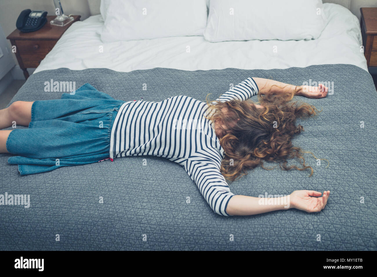 Une jeune femme épuisée n'est face sur le lit dans une chambre d'hôtel Banque D'Images