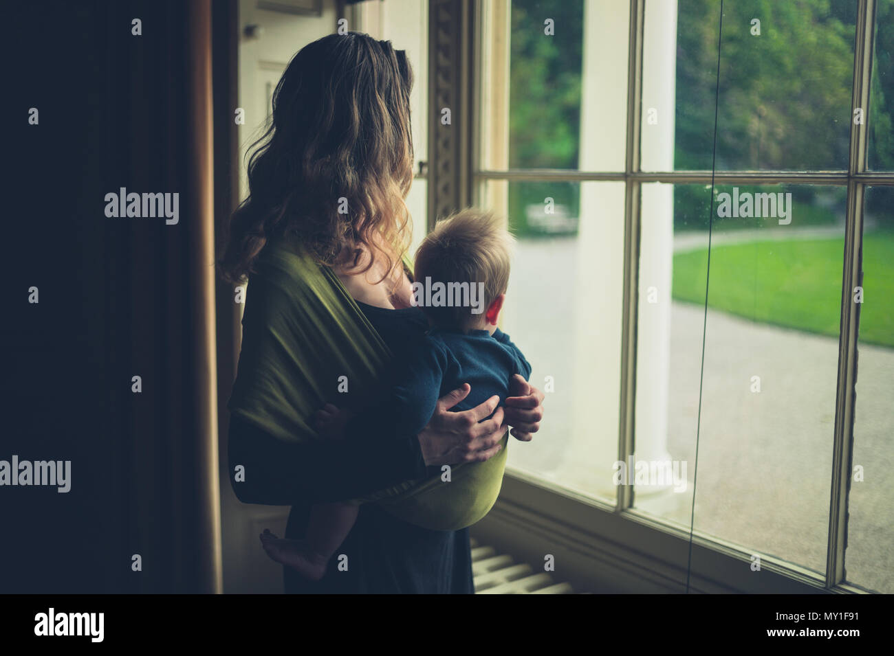Une mère avec un bébé dans une écharpe est debout près de la fenêtre dans un grand country house Banque D'Images