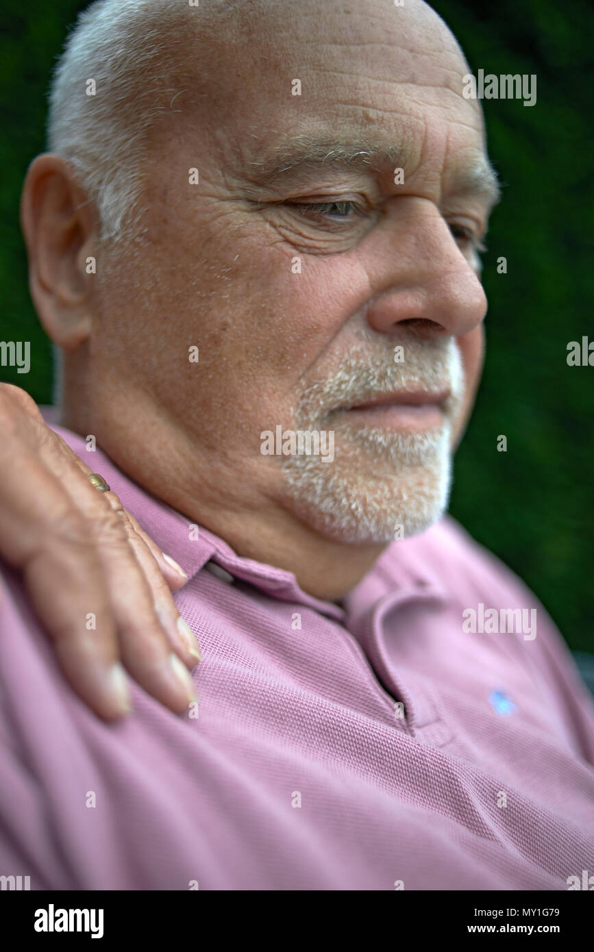 Portrait d'un homme âgé à la peur assis dehors dans le jardin avec la main de sa femme sur son épaule pour le réconforter en cas de besoin Banque D'Images