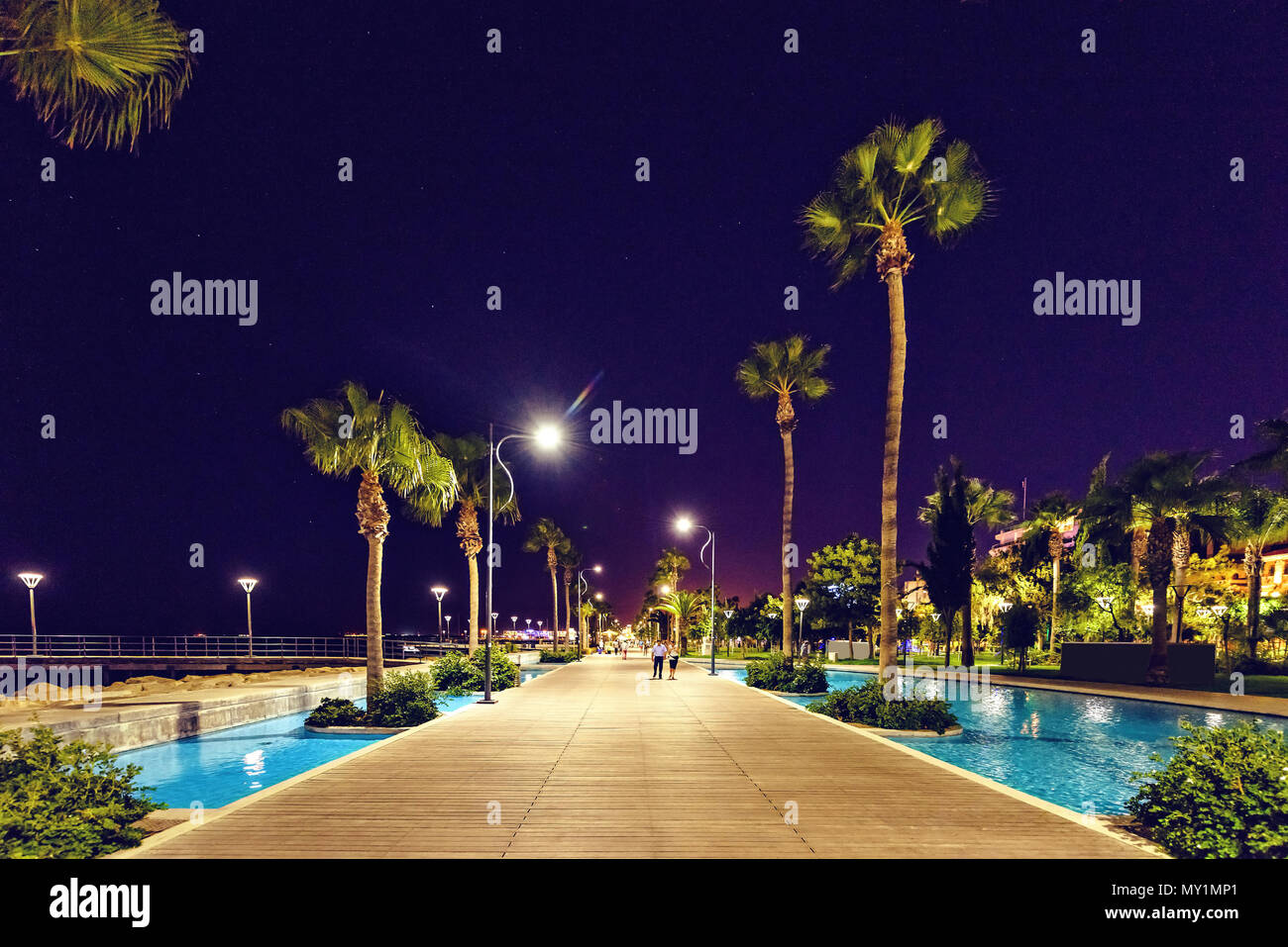 Vue de nuit, promenade alley avec de l'eau et de palmiers sur le côté. Des gens qui marchent. Copie négative de l'espace, place pour le texte. Limassol, Chypre Banque D'Images
