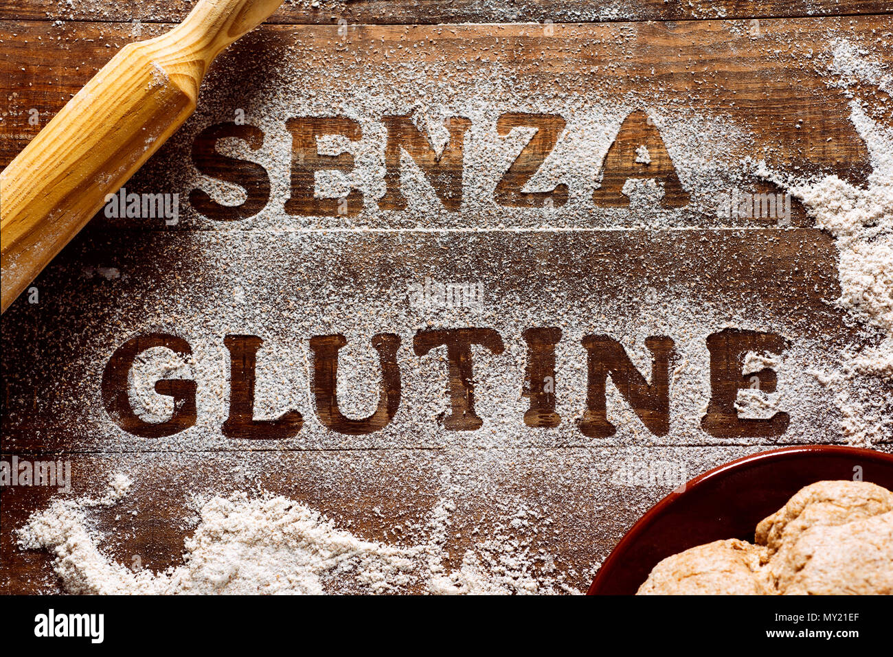 Portrait d'une table de bois arrosé avec une farine sans gluten où vous pouvez lire le texte senza glutine, sans gluten en italien, à côté d'un rouleau Banque D'Images