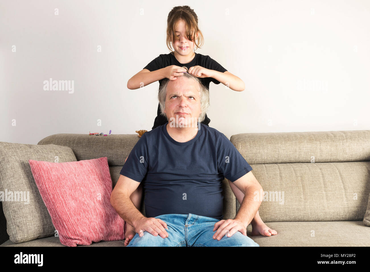 Petite Fille peignant et faire des tresses ou des nattes à son père sur le canapé à la maison Banque D'Images