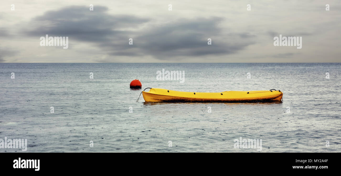Canoe jaune et rouge flottent sur la mer sur un temps maussade et humide journée d'hiver Banque D'Images