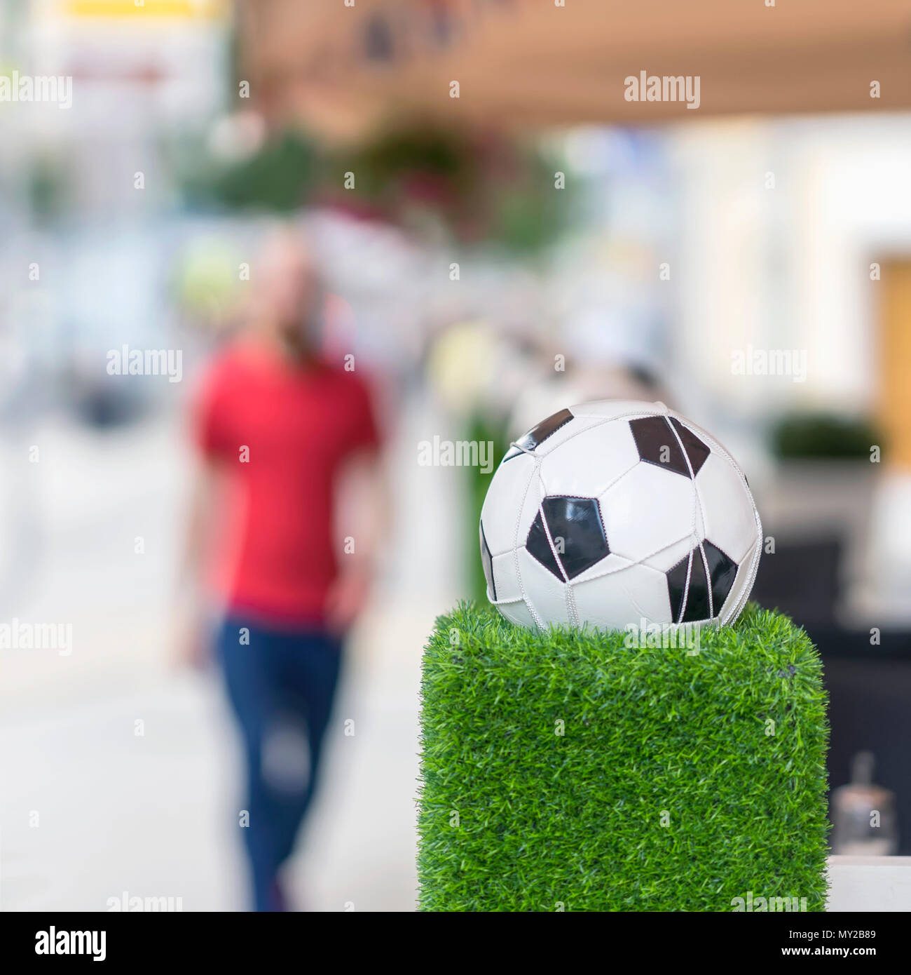 Stand de décoration sous la forme de la balle de football classique dans le filet sur l'herbe verte. Ornements des rues de la ville. L'homme trouble en rouge. Focu sélective Banque D'Images