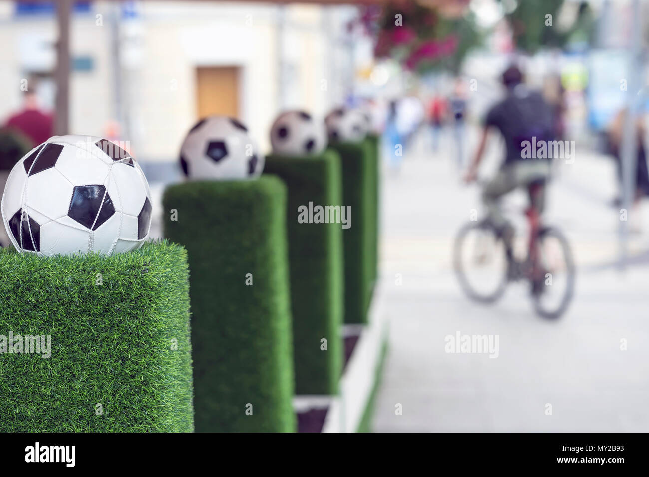 Stands de décoration avec ballon de foot dans le filet sur l'herbe verte. Ornements des rues de la ville. Les personnes floues, l'homme sur un vélo. Selective focus Banque D'Images