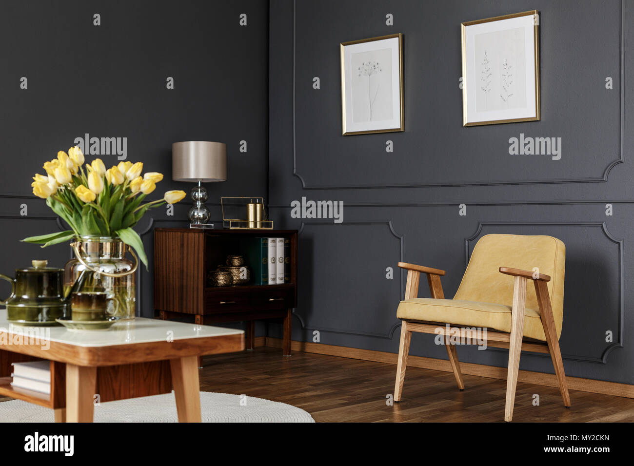 Armoire en bois dans le coin d'une salle de séjour avec boiseries d'intérieur avec des affiches sur le mur à côté d'un fauteuil et table jaune avec des tulipes. Banque D'Images