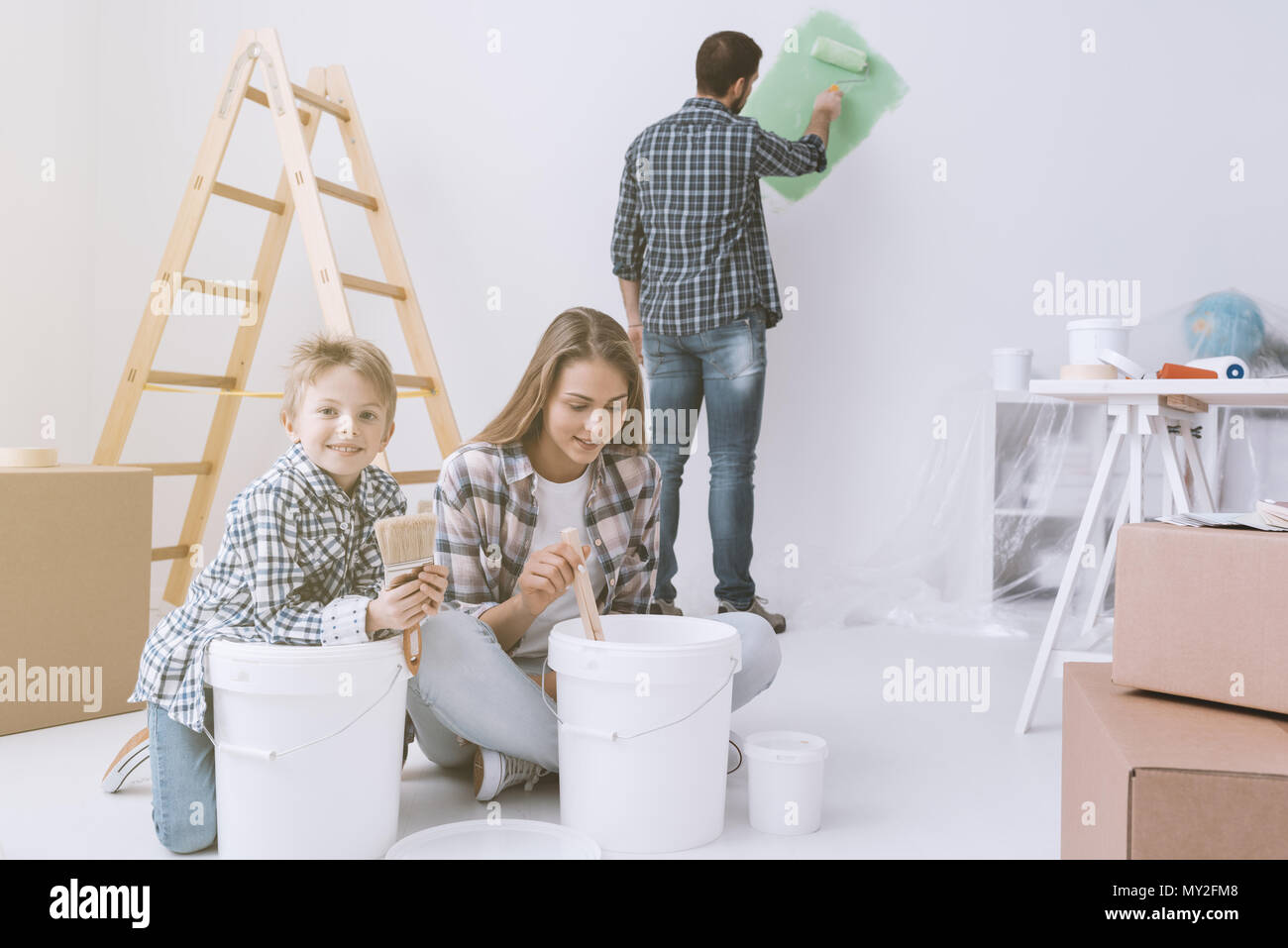 Jeune famille faire un Home makeover et peinture, le père est peinture des murs avec un rouleau à peindre, la mère et son fils sont en remuant en peinture Banque D'Images