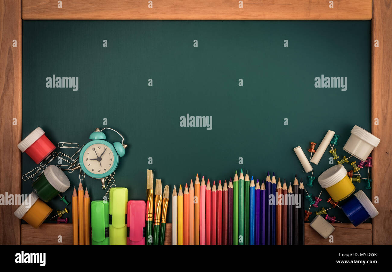 Réveil, peintures, crayons et papier vert de l'école sur tableau, vue de dessus Banque D'Images