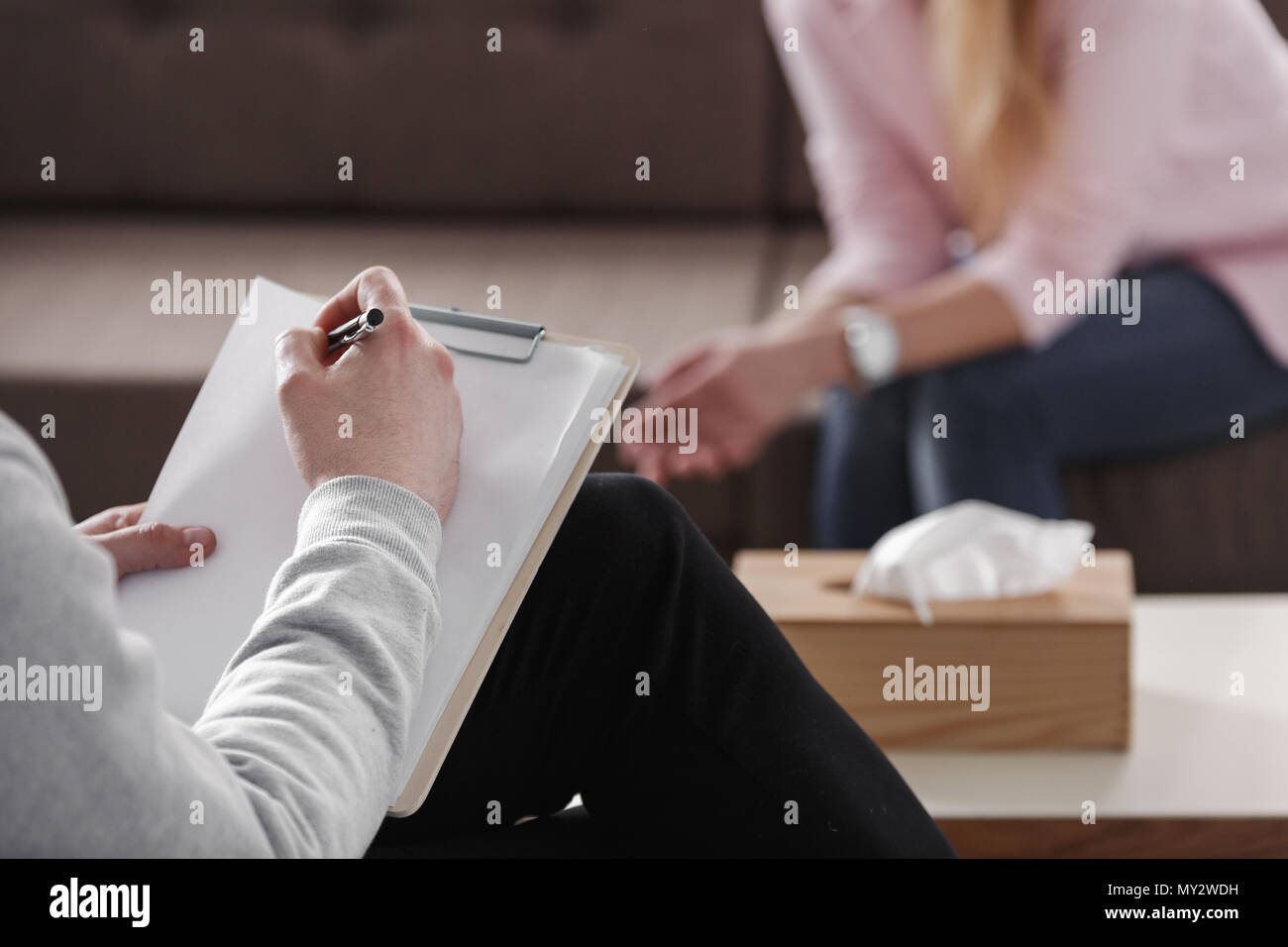 Close-up du thérapeute part la rédaction de notes au cours d'une séance de counseling avec une seule femme assise sur un canapé dans l'arrière-plan flou. Banque D'Images